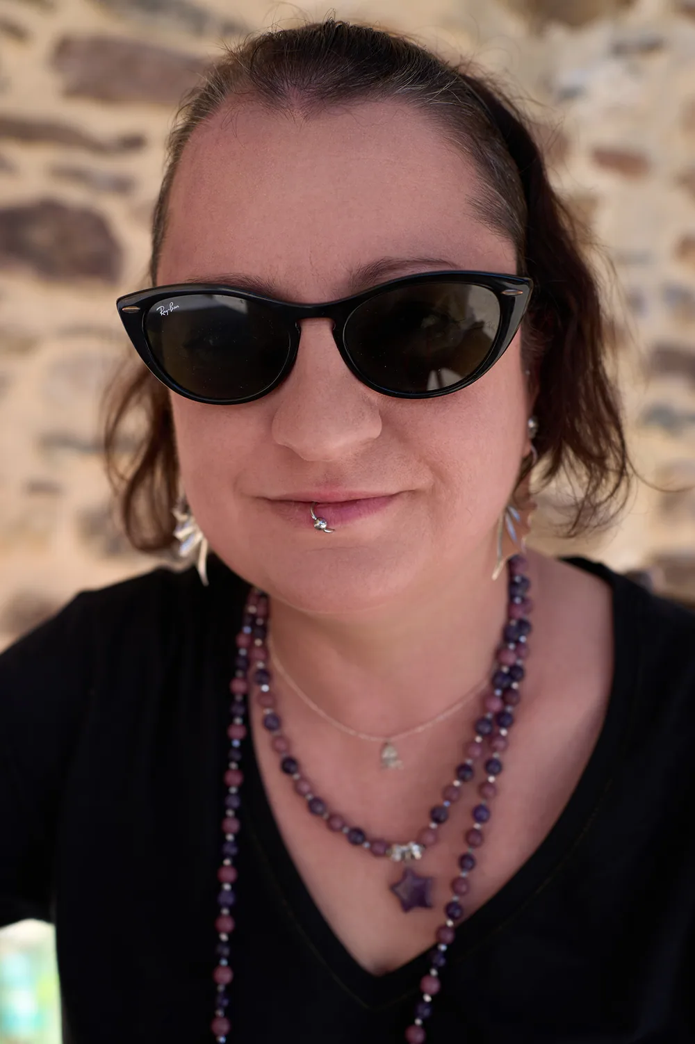 Portrait de Manuela Biocca, en lunettes de soleil noires et collier de perles violettes