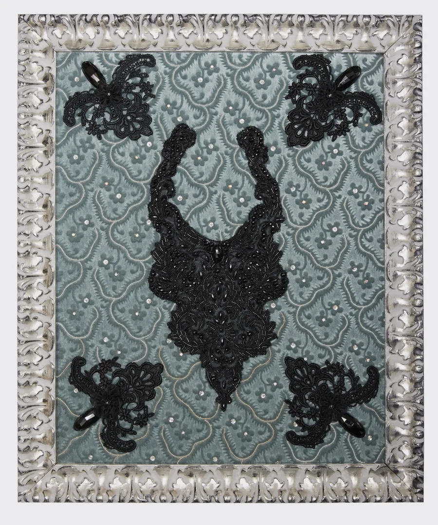 Collier brodé de perles et de cabochons noirs sur un fond gris-bleu, cadre argenté