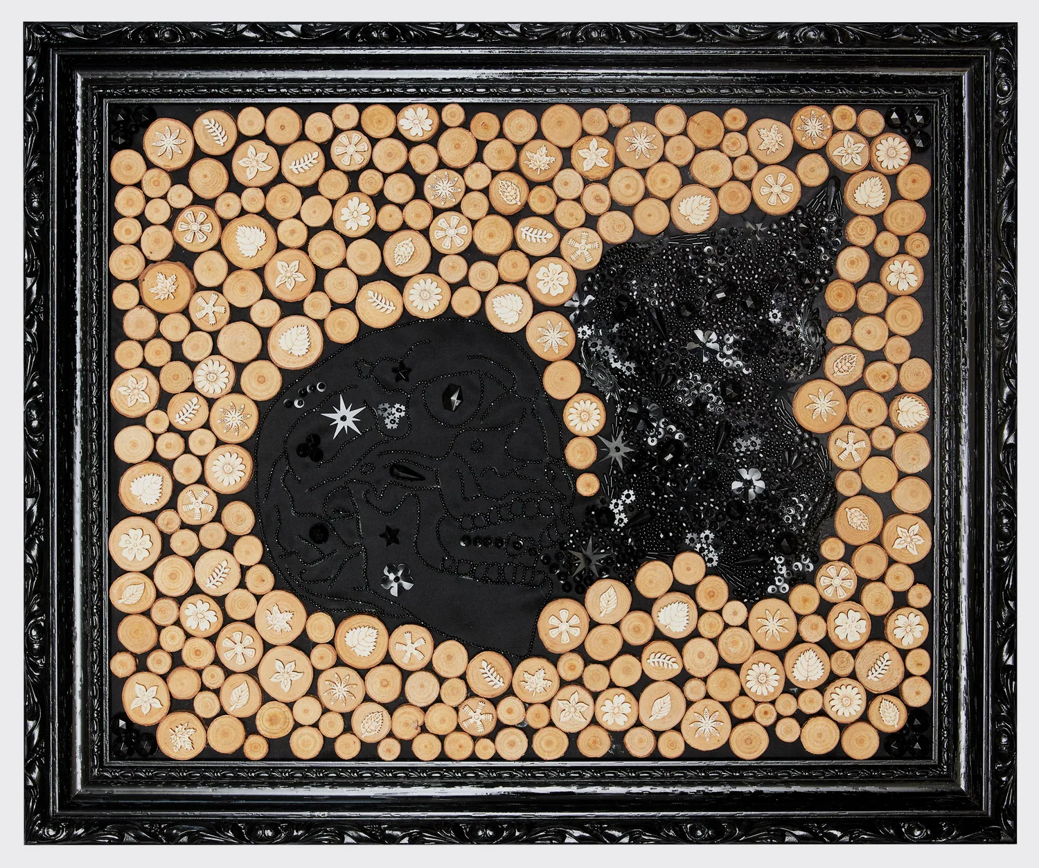 Tête de mort brodée de perles noires entourée de rondins de bois, de feuilles et de fleurs en bois, cadre noir