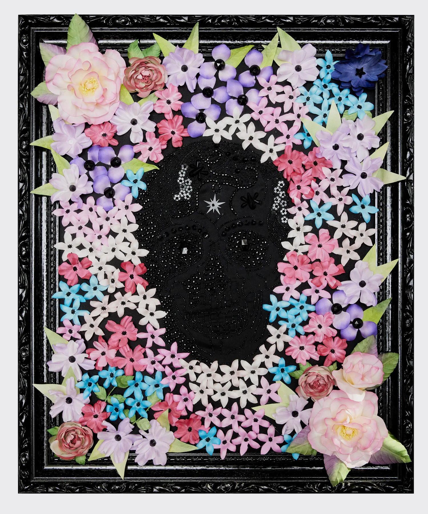 Tête de mort brodée de perles noires entourée de fleurs en soie roses, violettes et bleues, cadre noir