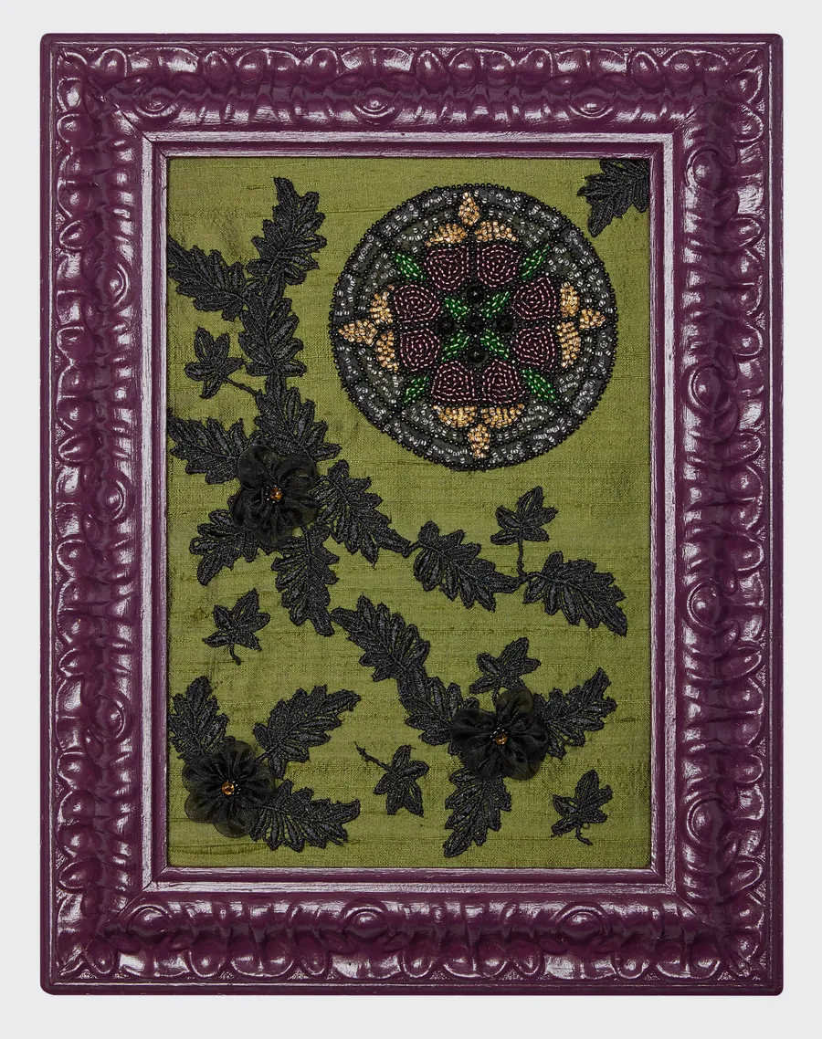 Petit vitrail circulaire en perles entouré de feuilles de dentelle noire sur fond vert, cadre violet